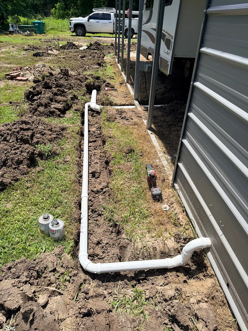 Long exterior PVC drain line run trenched alongside a building