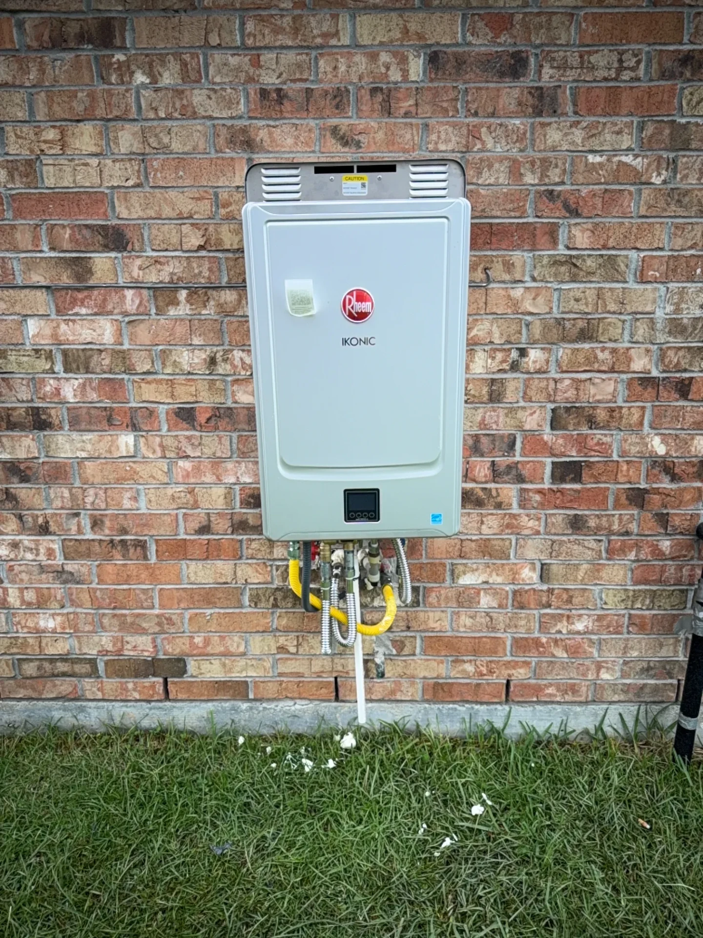 Rheem Ikonic tankless water heater mounted on an exterior brick wall